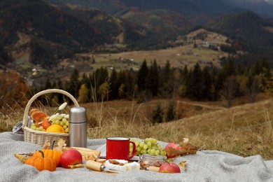 Photo of Blanket with picnic basket, snacks and autumn leaves in mountains, space for text