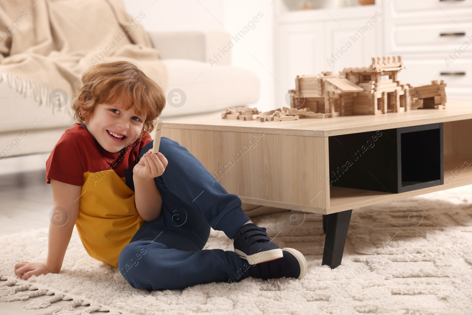 Photo of Cute little boy playing with wooden construction set on carpet at home. Child's toy