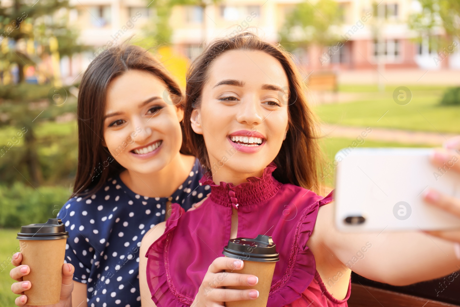 Photo of Young women with cups of coffee taking selfie outdoors