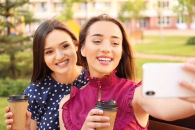 Young women with cups of coffee taking selfie outdoors