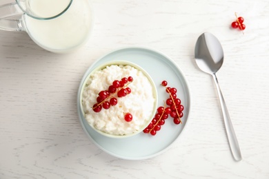 Photo of Creamy rice pudding with red currant in bowl served on white wooden table, top view