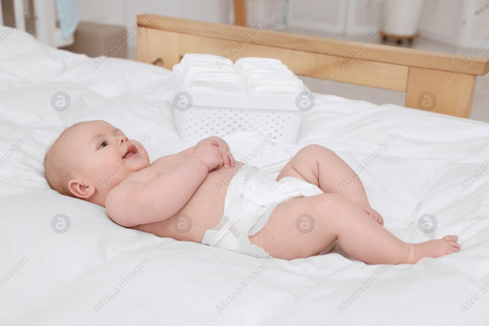 Photo of Cute baby and diapers on white bed at home