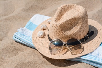 Straw hat with seashells, sunglasses and beach towel on sand