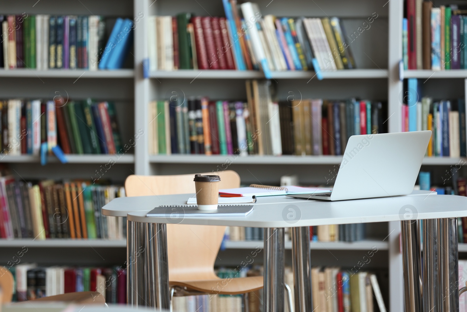 Photo of Laptop, drink and stationery on table in library