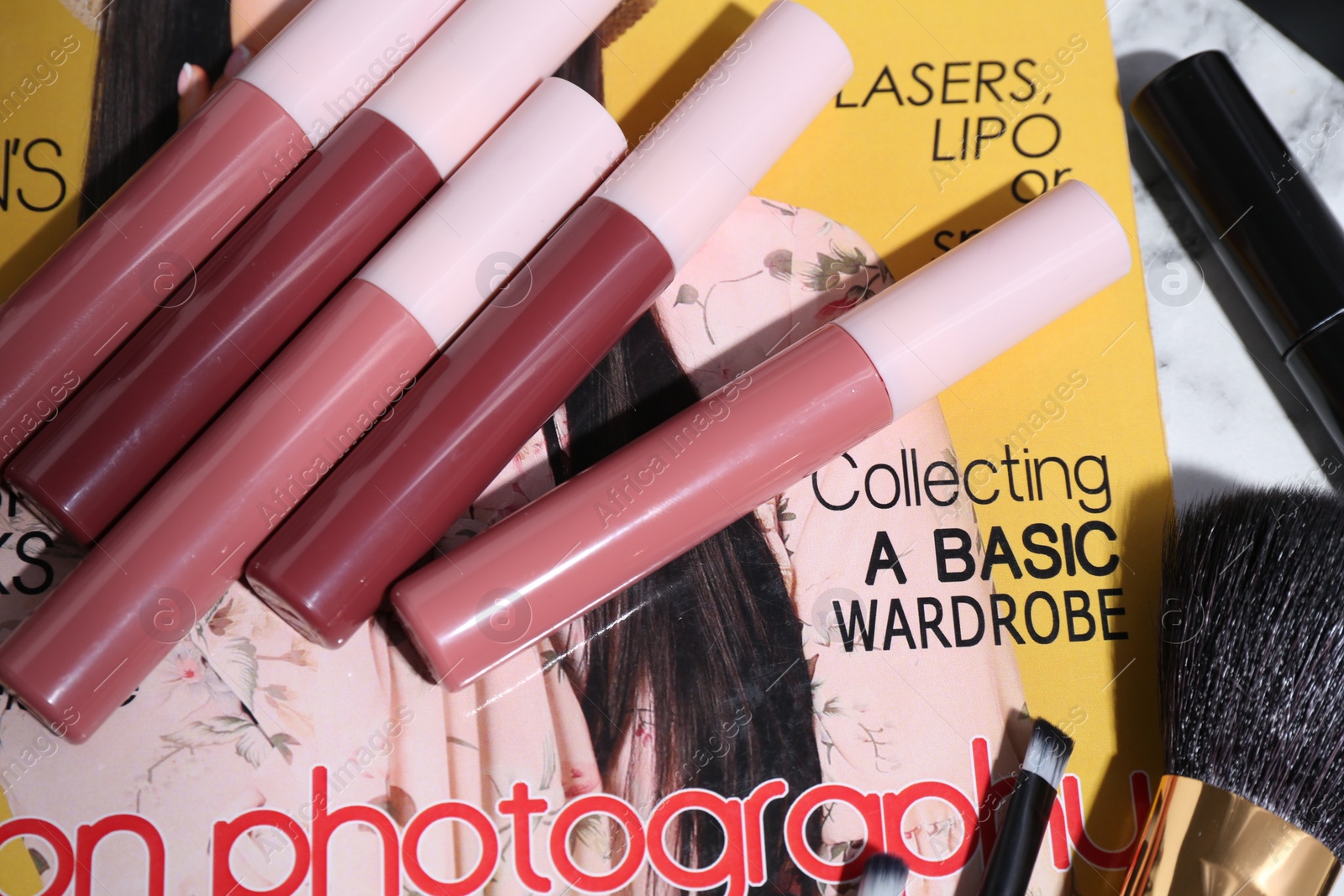 Photo of Bright lip glosses and fashion magazine on table, closeup
