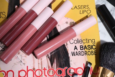 Bright lip glosses and fashion magazine on table, closeup