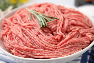 Photo of Fresh raw ground meat and rosemary in bowl on table, closeup