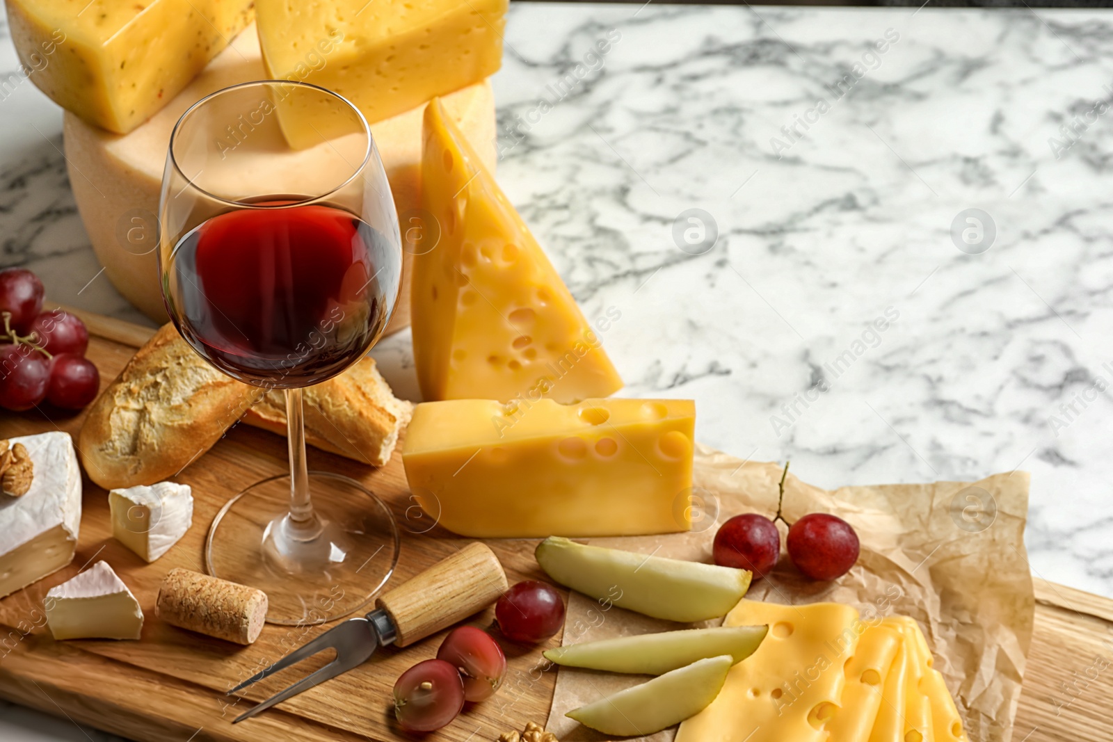 Photo of Board with different kinds of delicious cheese, snacks and wine on marble table. Space for text