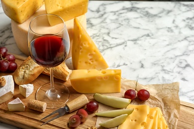 Board with different kinds of delicious cheese, snacks and wine on marble table. Space for text