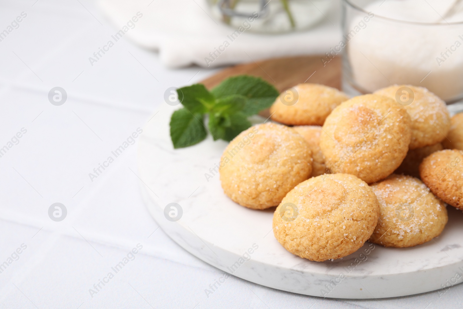 Photo of Tasty sweet sugar cookies, milk and mint on white tiled table, closeup. Space for text