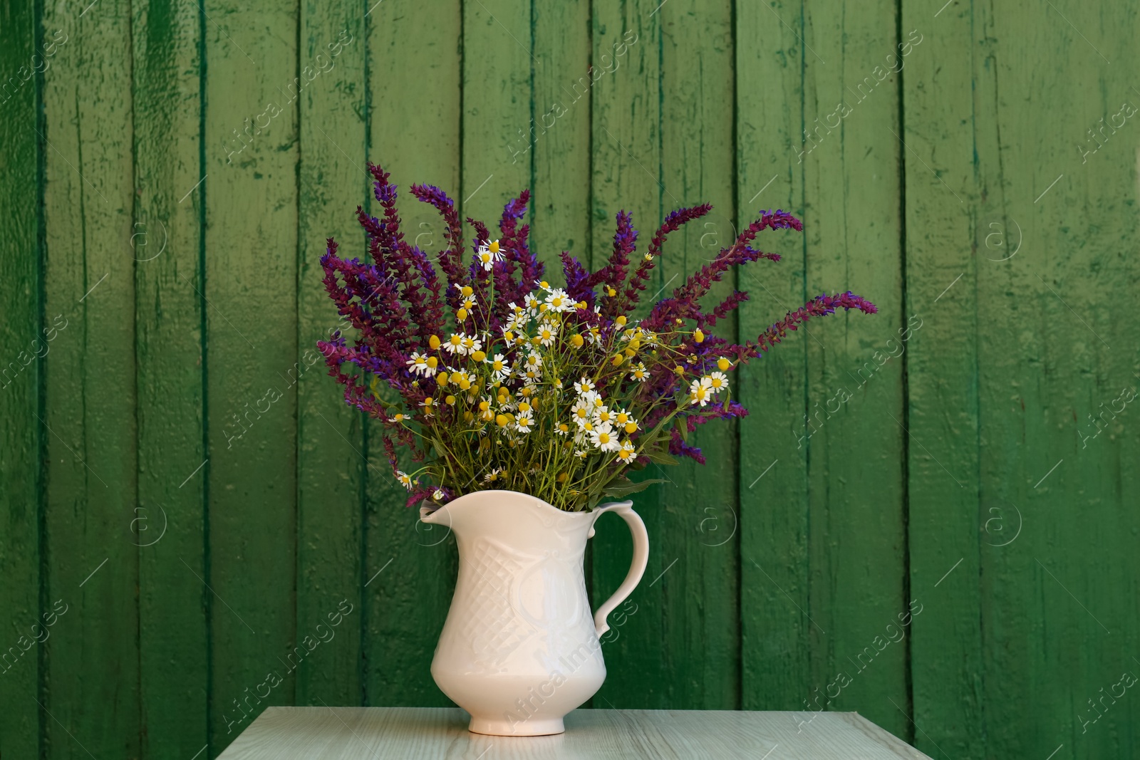 Photo of Beautiful bouquet with field flowers in jug on white wooden table