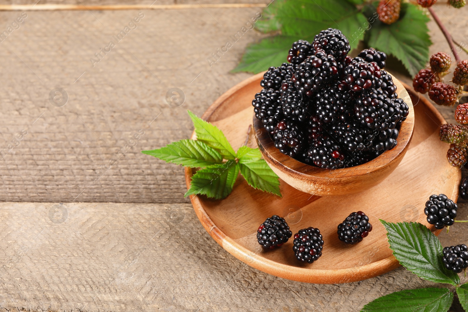 Photo of Fresh ripe blackberries and leaves on wooden table. Space for text