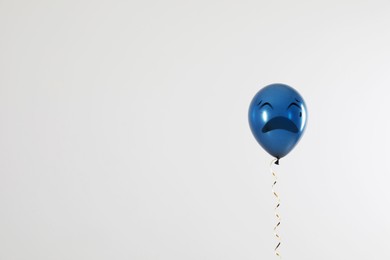 Blue balloon with sad face on light grey background. Space for text