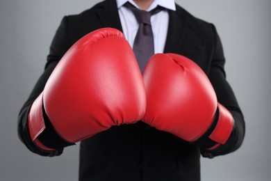 Photo of Businessman in suit wearing boxing gloves on grey background, closeup