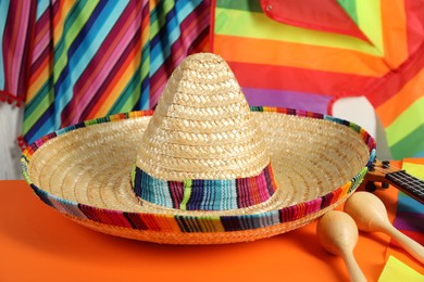 Photo of Mexican sombrero hat and maracas on orange table, closeup