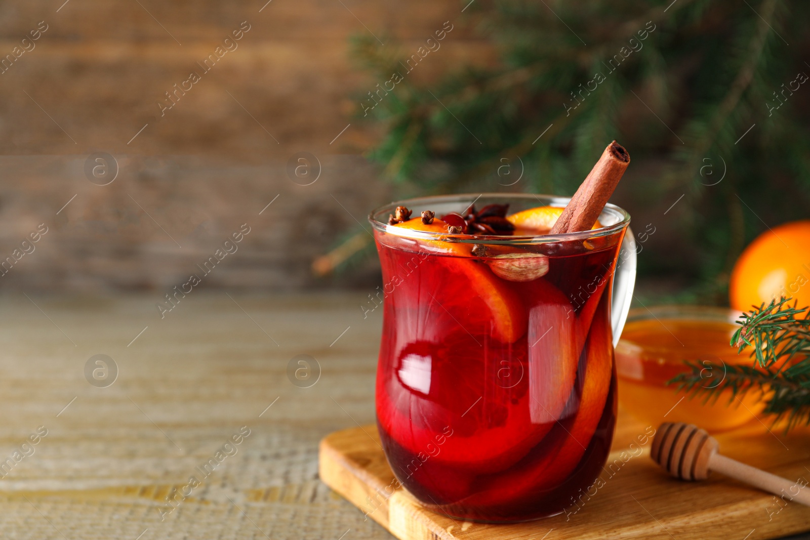 Photo of Glass cup of tasty mulled wine on wooden table. Space for text