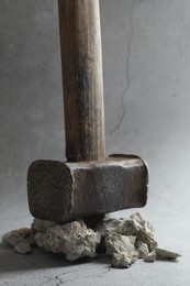 Photo of One sledgehammer and pieces of broken stones on grey background, closeup