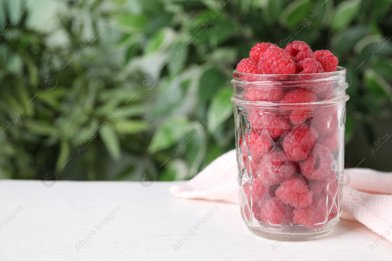 Photo of Delicious fresh ripe raspberries in glass jar on white wooden table. Space for text