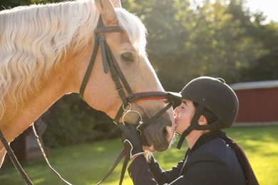 Photo of Young woman in horse riding suit and her beautiful pet outdoors on sunny day