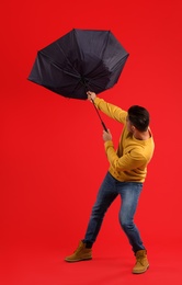 Photo of Man with umbrella caught in gust of wind on red background