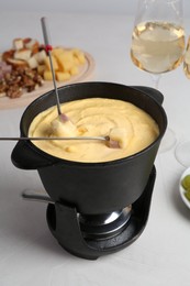 Fondue pot with tasty melted cheese, forks, ham and wine on white table