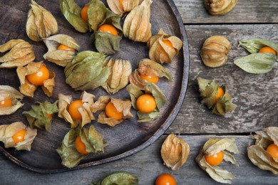 Ripe physalis fruits with dry husk on wooden table, flat lay