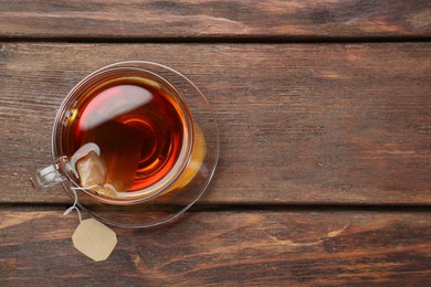 Photo of Brewing aromatic tea. Cup with teabag on wooden table, top view. Space for text