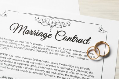 Marriage contracts and gold rings on light wooden table, top view