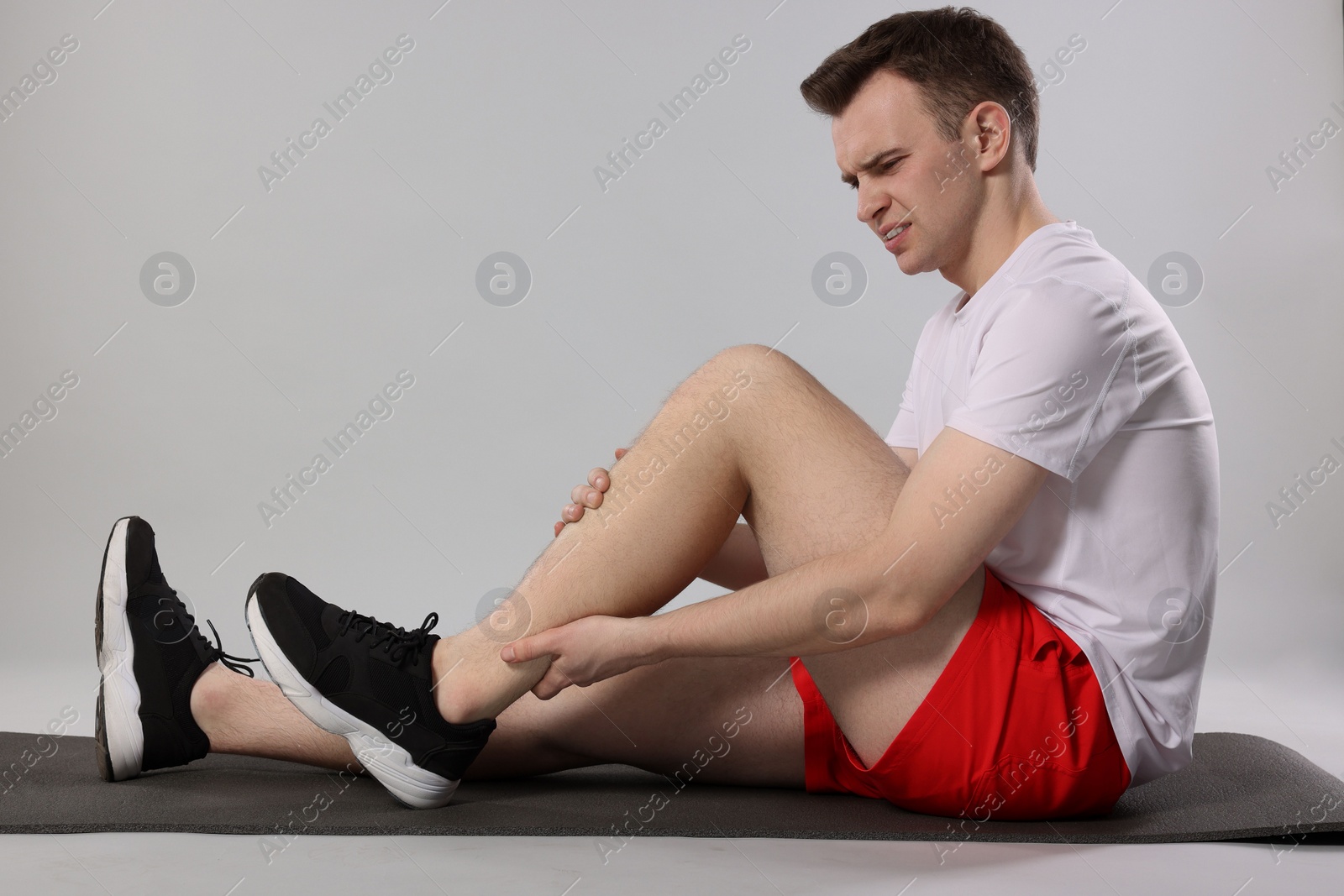 Photo of Man suffering from leg pain on mat against grey background