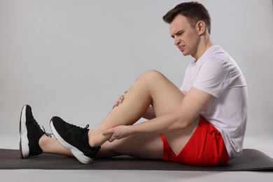 Man suffering from leg pain on mat against grey background