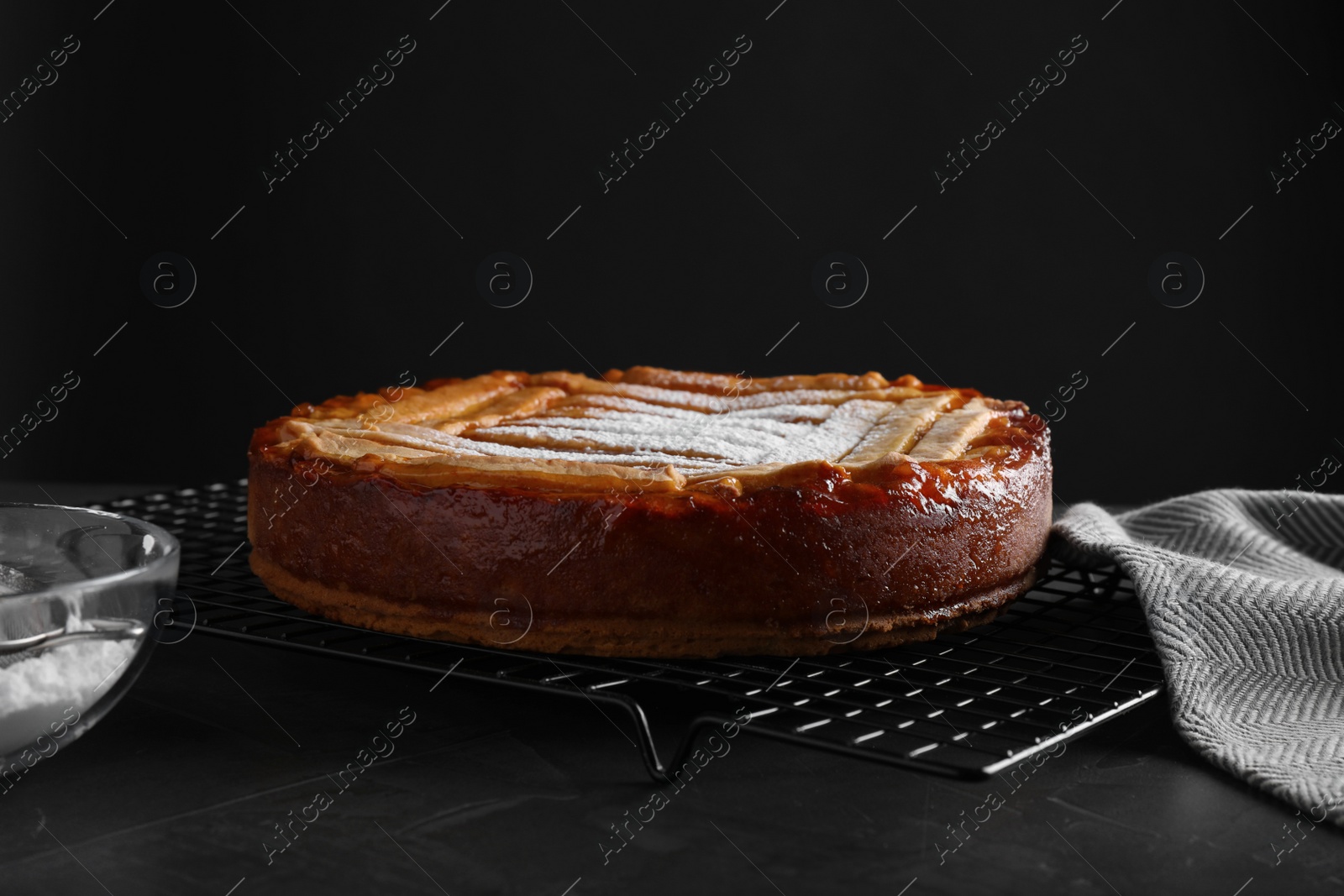 Photo of Tasty apricot pie with powdered sugar on table against black background