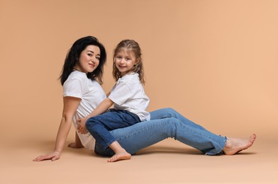 Photo of Beautiful mother with little daughter sitting on beige background