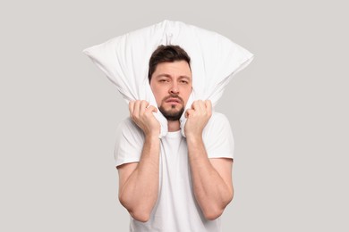 Tired man covering ears with pillow on light grey background. Insomnia problem