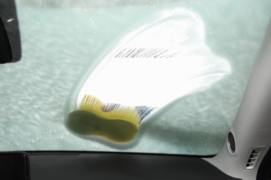 Photo of Worker cleaning automobile windshield with sponge at car wash, view from inside