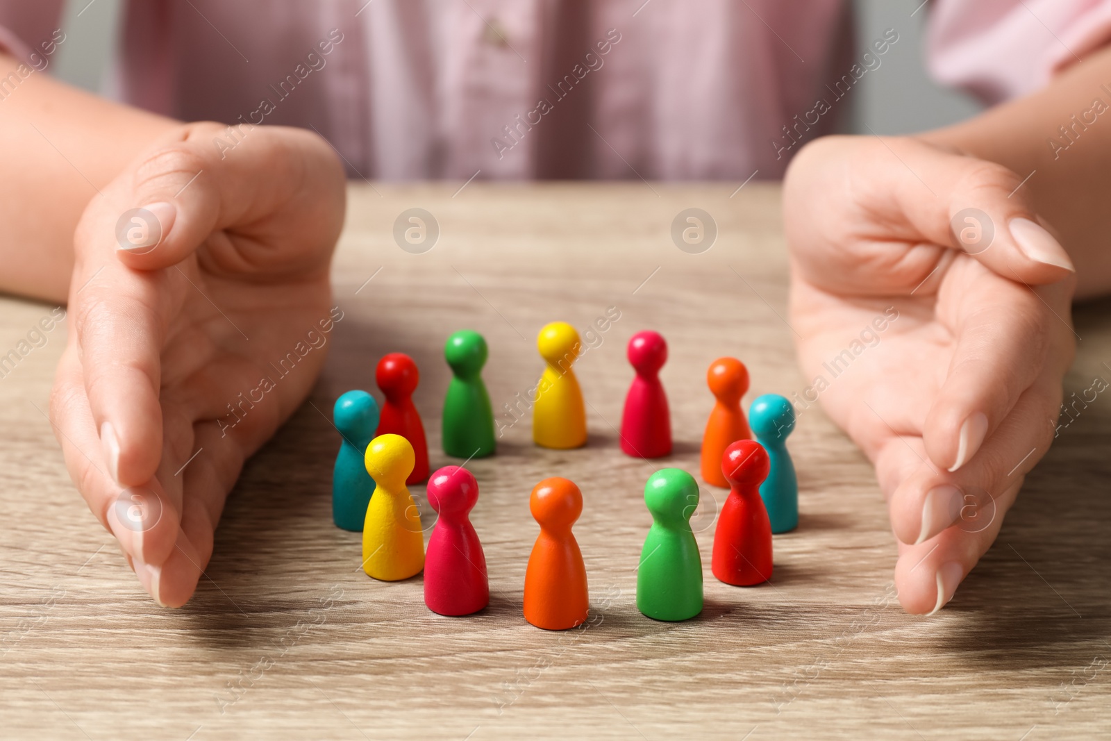 Photo of Woman protecting colorful pawns at wooden table, closeup. Social inclusion concept