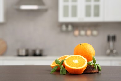 Whole and cut oranges on wooden counter in kitchen, space for text