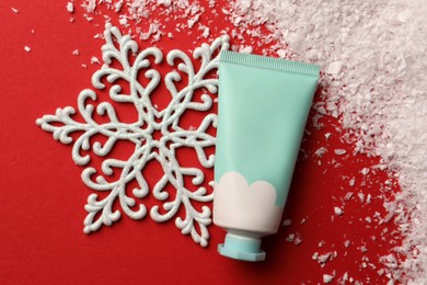 Photo of Winter skin care. Hand cream and artificial snow on red background, flat lay