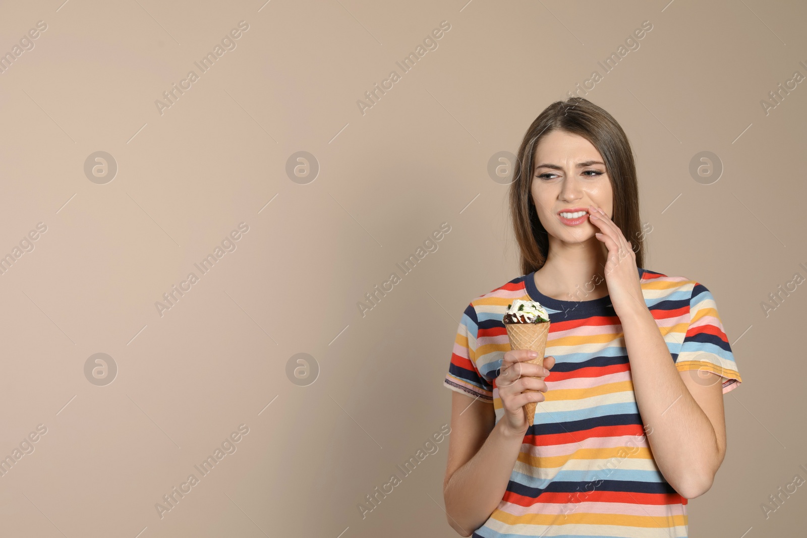 Photo of Emotional young woman with sensitive teeth and ice cream on color background. Space for text