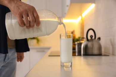 Man pouring milk from gallon bottle into glass at white countertop in kitchen, closeup