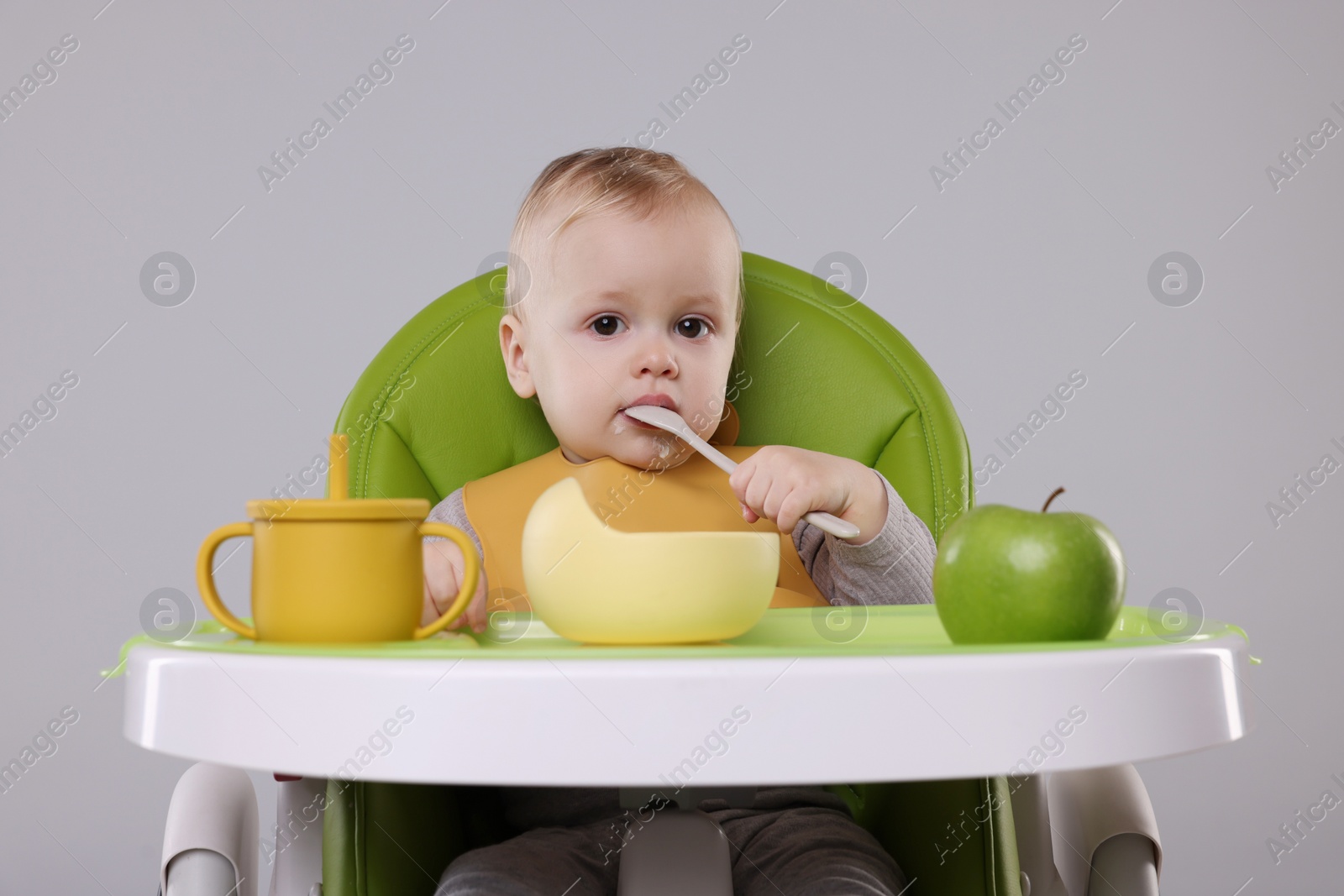 Photo of Cute little baby eating healthy food in high chair on gray background