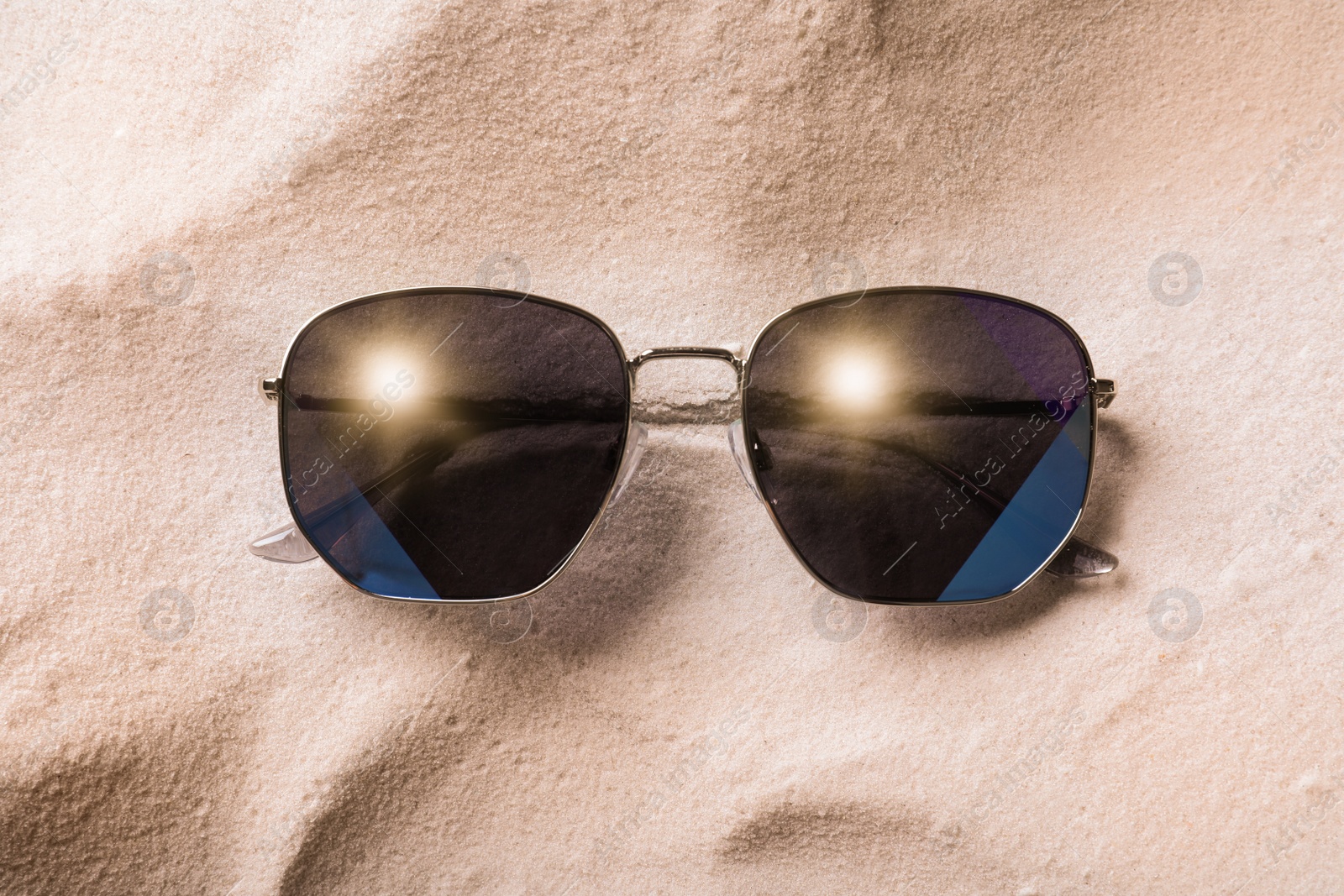 Photo of Stylish sunglasses on white sand, top view