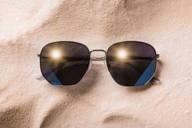 Photo of Stylish sunglasses on white sand, top view