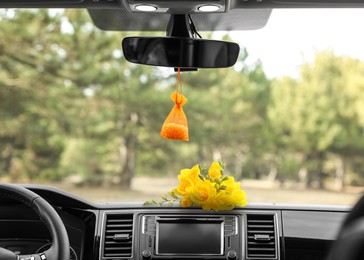 Beautiful flowers and air freshener hanging on rear view mirror in car