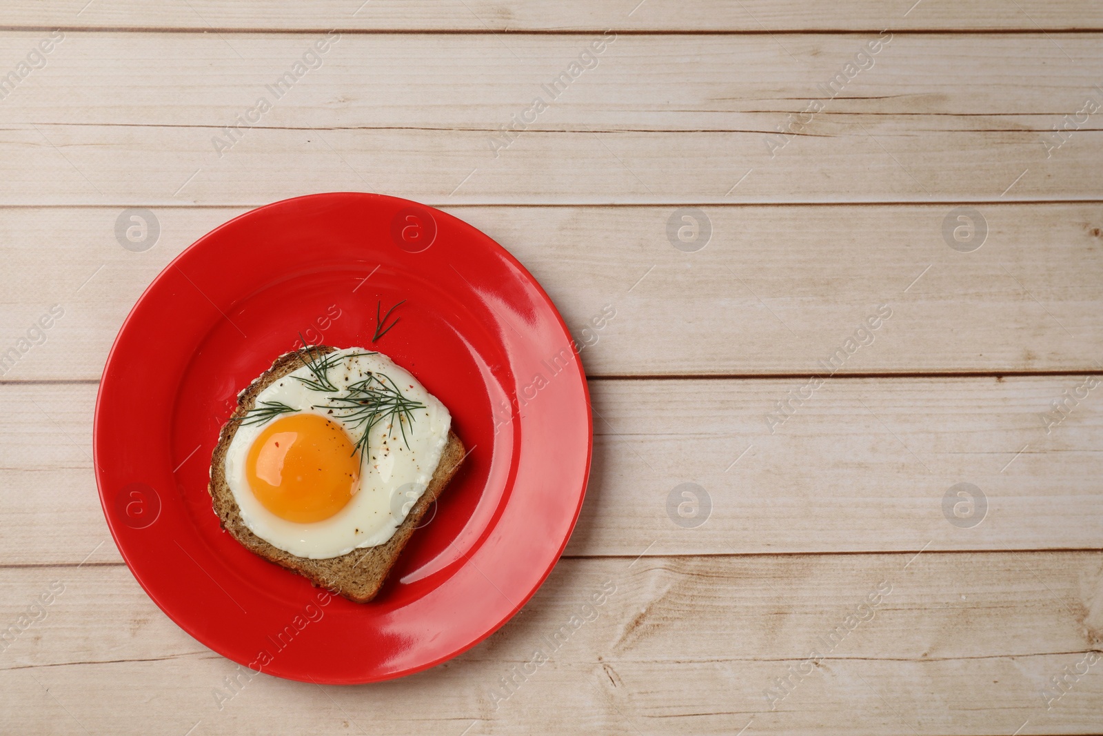 Photo of Plate with tasty fried egg, slice of bread and dill on light wooden table, top view. Space for text