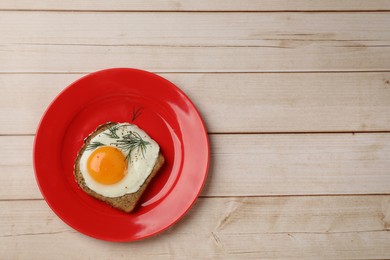 Photo of Plate with tasty fried egg, slice of bread and dill on light wooden table, top view. Space for text