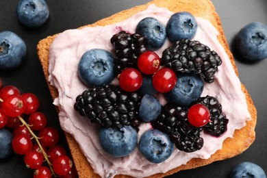 Tasty sandwiches with cream cheese and berries on black plate, flat lay