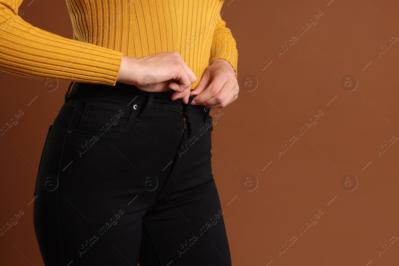 Photo of Woman wearing stylish black jeans on brown background, closeup. Space for text