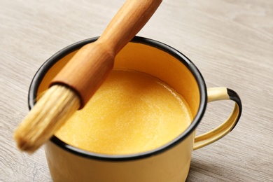 Mug of melting butter with brush on wooden table, closeup