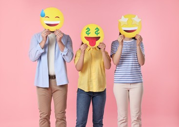 People covering faces with emoticons on pink background