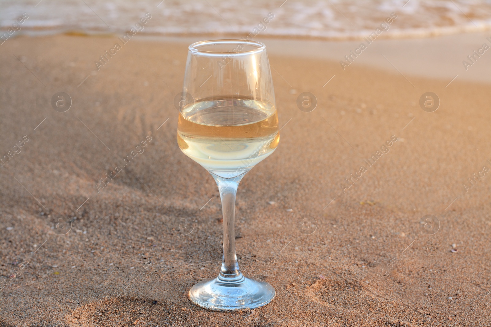 Photo of Glass of tasty wine on sand near sea